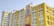 Several modern buildings with yellow and white facades stand under a clear sky. One of the buildings features a colorful mural, and another has a sign for Kailash Deepak Hospital.