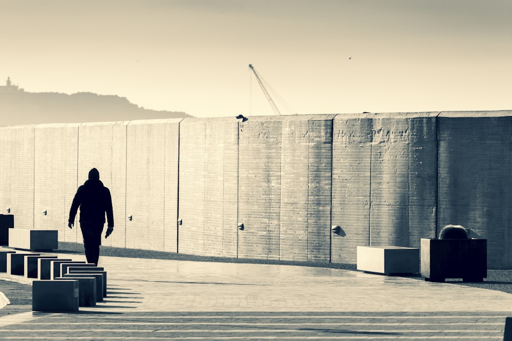 a man walking in front of a large concrete wall