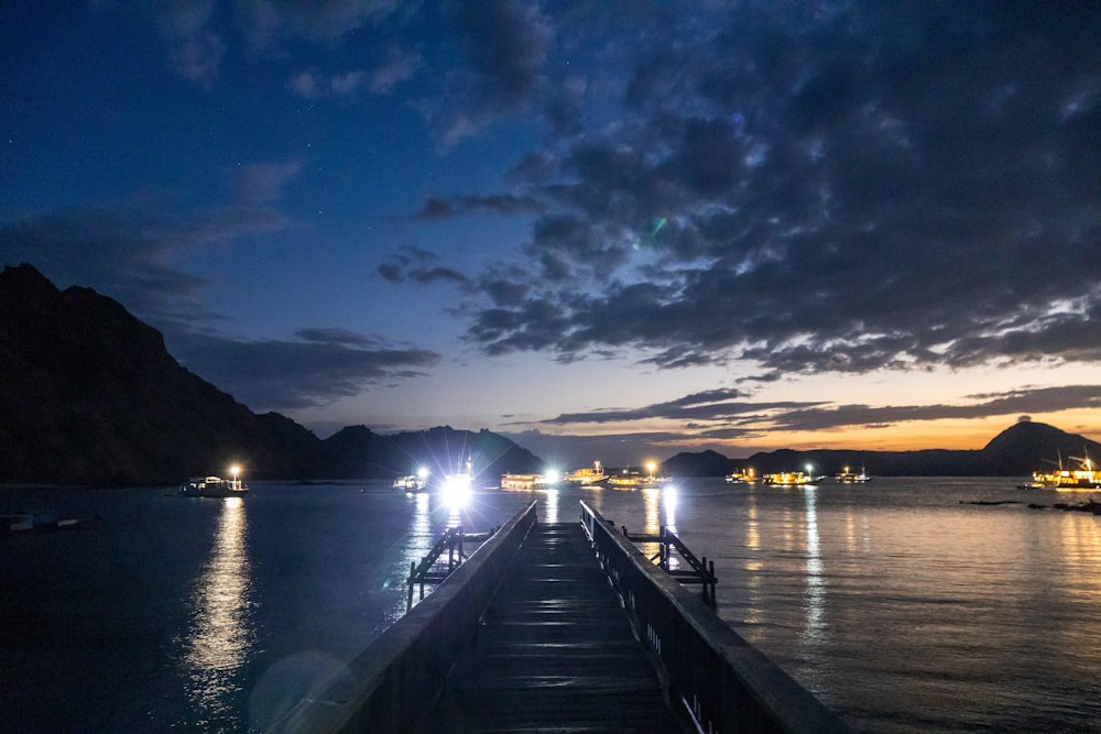 a dock with lights on it by water with mountains in the background