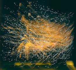 A dynamic explosion of light trails and spark-like patterns appears against a dark background, creating an intricate and flowing visual effect.