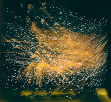 A dynamic explosion of light trails and spark-like patterns appears against a dark background, creating an intricate and flowing visual effect.