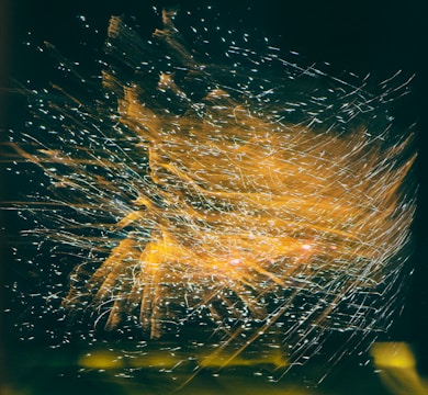A dynamic explosion of light trails and spark-like patterns appears against a dark background, creating an intricate and flowing visual effect.