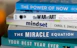 A stack of self-help and motivational books with colorful covers is neatly arranged. The titles include 'The Power of Now', 'The War of Art', 'Mindset', 'The Miracle Equation', and 'Your Best Year Ever'.