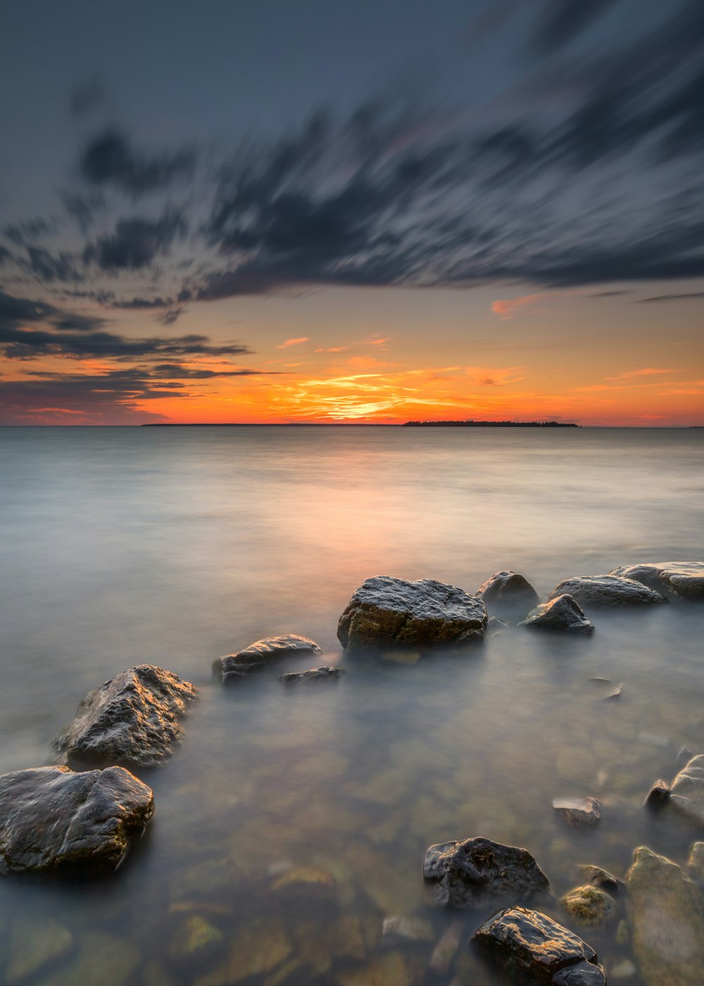 un cuerpo de agua con rocas y una puesta de sol