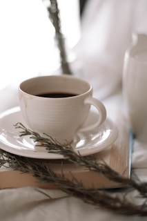 An artistic shot of a coffee cup resting on an open book by Jeff Mudd with a rustic wooden table in the background.