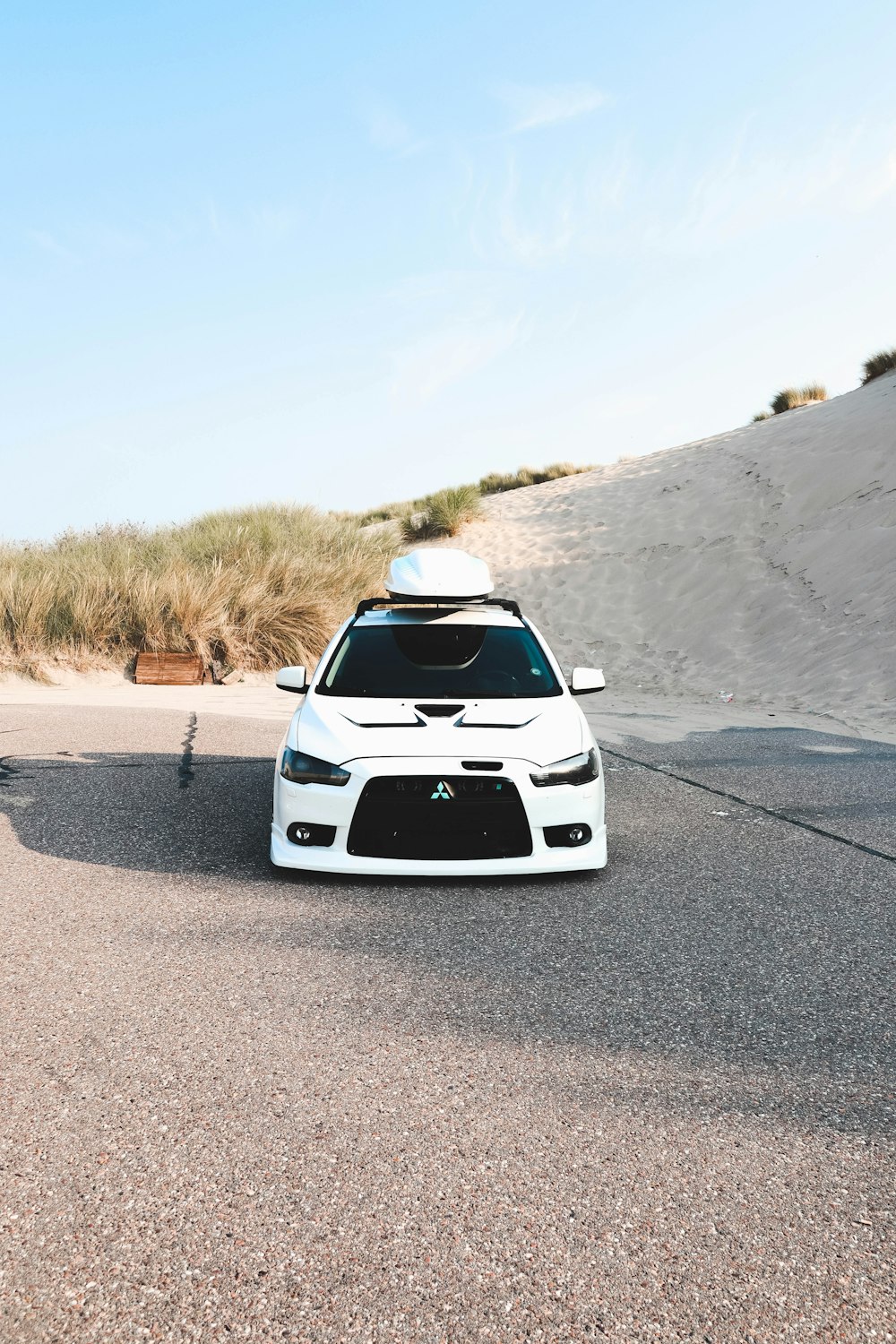 a white car with a white top on a road with sand and bushes