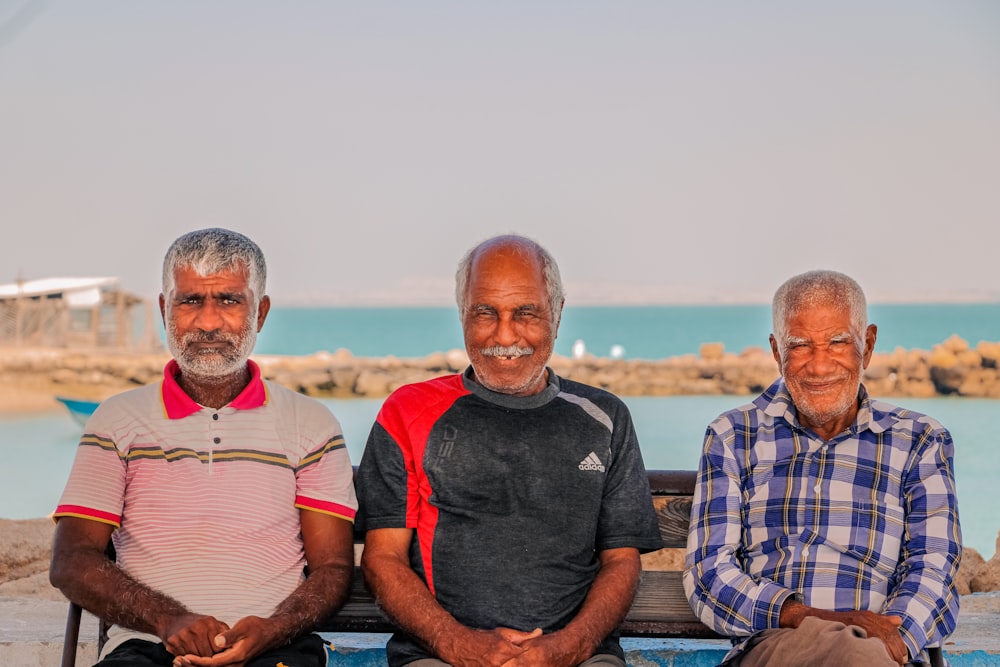 a group of men sitting on a bench in front of a body of water