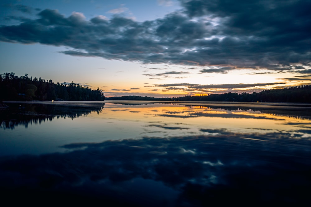 a body of water with trees and a sunset in the background