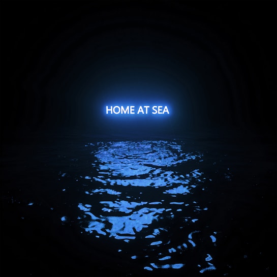 A dark scene featuring a body of water illuminated by a bright blue light with the words 'HOME AT SEA' reflected on the surface, creating a serene and mysterious atmosphere.