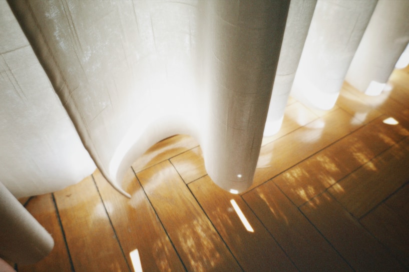 Soft morning light filters through sheer curtains into a serene pilates studio with muted sage walls.