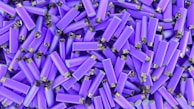 A large collection of identical purple lighters with silver tops piled on top of each other in a random pattern.