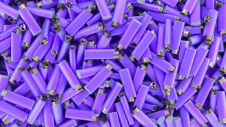 A large collection of identical purple lighters with silver tops piled on top of each other in a random pattern.