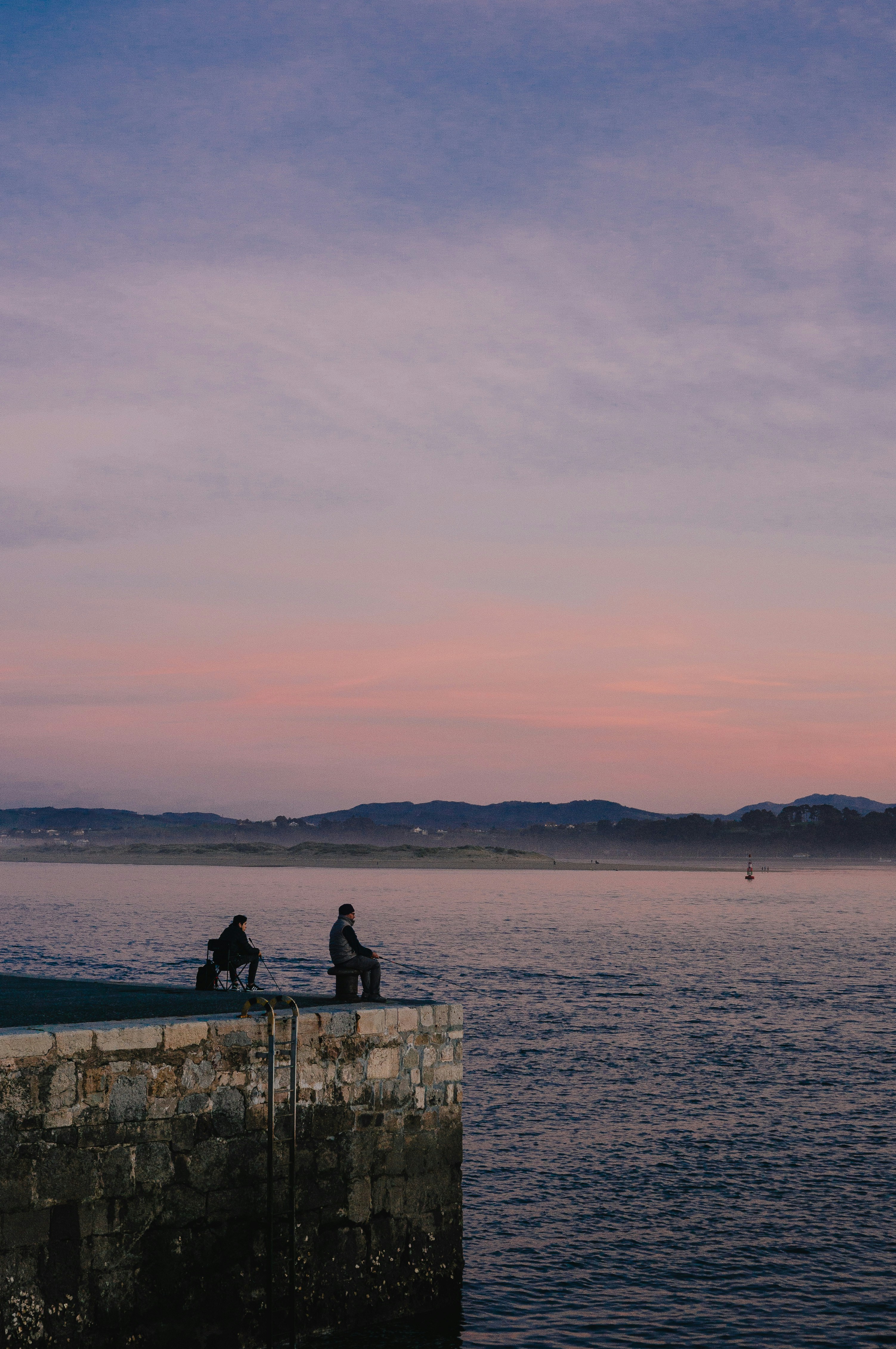 un paio di persone sedute su un muro di pietra che si affaccia su uno specchio d'acqua