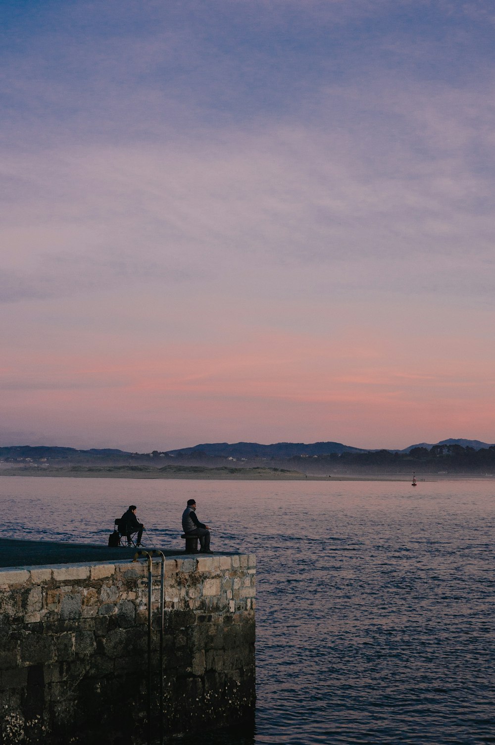 a couple of people sitting on a stone wall overlooking a body of water
