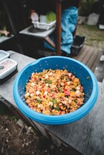 A colorful bowl of fresh mixed vegetables and grains on a rustic table.