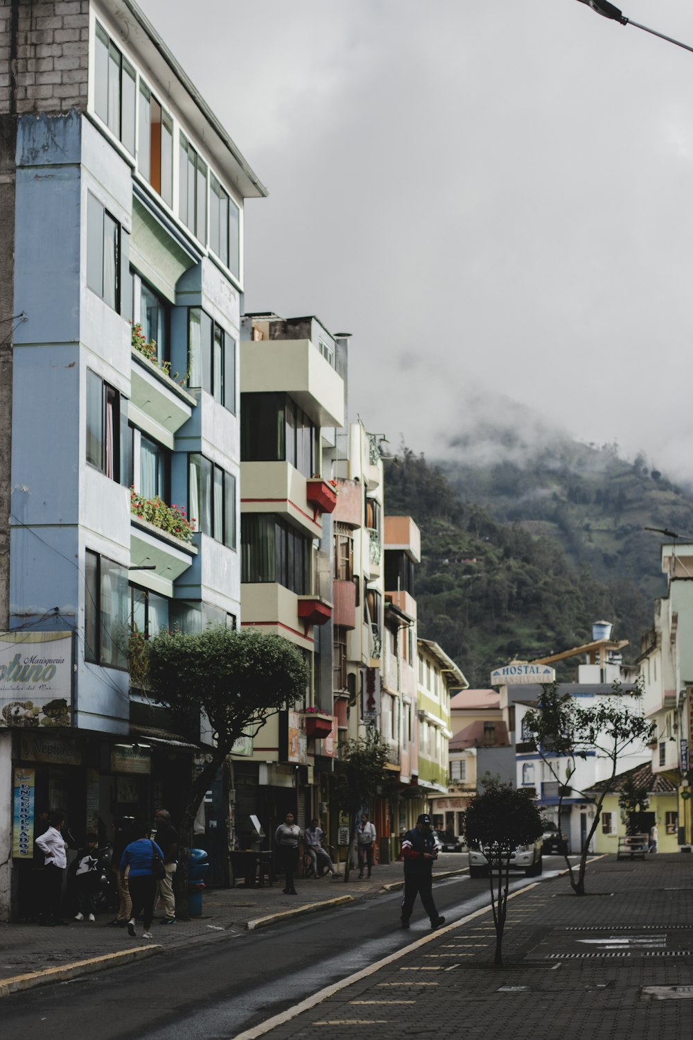 uma rua com edifícios e pessoas sobre ela com uma montanha ao fundo