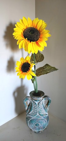 A tall, slender vase with a narrow neck displaying a single sunflower against a bright, airy background.