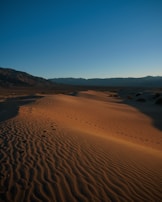 Close-up of sandboarders' feet carving through soft sand dunes at sunset.