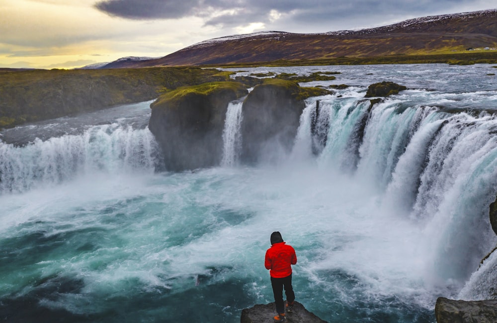 a person standing on a rock looking at a large waterfall