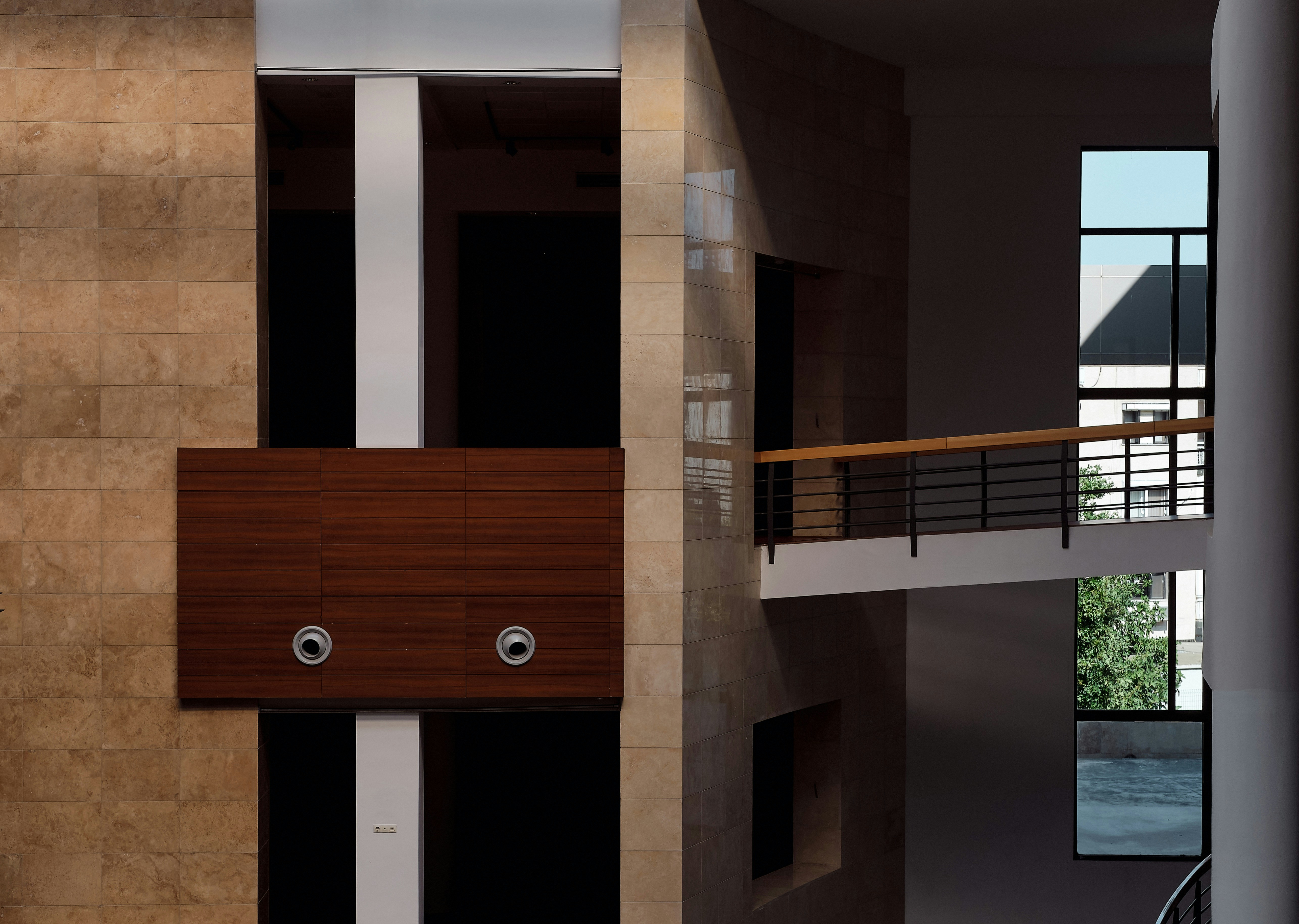 Modern interior architecture with textured stone walls, dark wood paneling, white pillars, and a connecting bridge, featuring geometric shapes and stark contrasts.