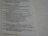 A close-up view of a printed page containing text in poetic format. The text appears to be organized in verses or stanzas, containing religious or spiritual content. The font is clear, and the page has margins with dotted lines on the side, possibly indicating space for notes.