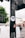 A black traffic light pole with a Hertha BSC sticker and a cat sticker is in the foreground. The background features a blurred white van passing by, green trees, and a row of white and red buildings under a cloudy sky.