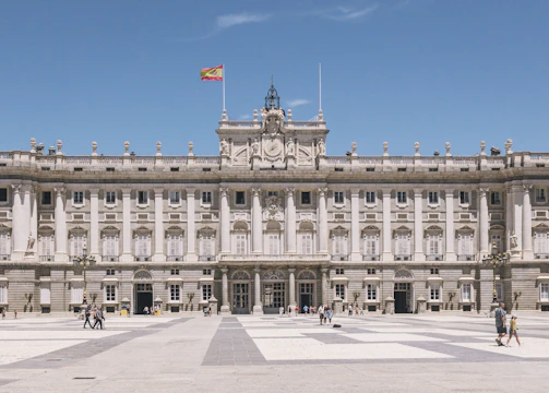 a large building with columns and a flag on top with Royal Palace of Madrid in the background