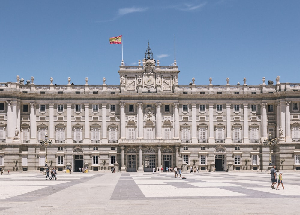 a large building with columns and a flag on top with Royal Palace of Madrid in the background