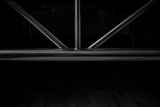 Metal rods form a geometric pattern, likely part of a structure or furniture piece, set against a dark background.