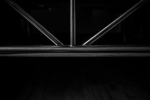 Metal rods form a geometric pattern, likely part of a structure or furniture piece, set against a dark background.