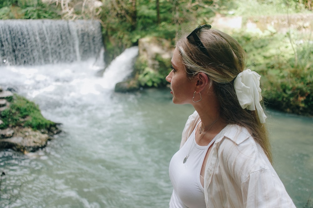 a woman in a white dress looking at a waterfall