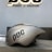 A sleek, metallic gray helmet with a streamlined design is placed on a textured surface. The helmet has the letters 'POC' and the phrase 'Power of Creation' printed on its side in black. Behind the helmet, the same 'POC Power of Creation' text is illuminated on a gray wall.