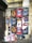 A wall covered with a collage of various posters featuring different designs and advertisements. The posters predominantly advertise 'Craft Cocktails' with artistic portraits and vibrant text, suggesting themes of nightlife or beverages. Some of the posters are torn or overlapped, showing signs of wear and urban decay. The wall itself is weathered, with visible graffiti above the posters.
