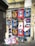 A wall covered with a collage of various posters featuring different designs and advertisements. The posters predominantly advertise 'Craft Cocktails' with artistic portraits and vibrant text, suggesting themes of nightlife or beverages. Some of the posters are torn or overlapped, showing signs of wear and urban decay. The wall itself is weathered, with visible graffiti above the posters.