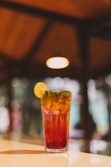 A vibrant glass of colorful welcome drink garnished with a slice of lemon and mint leaves.