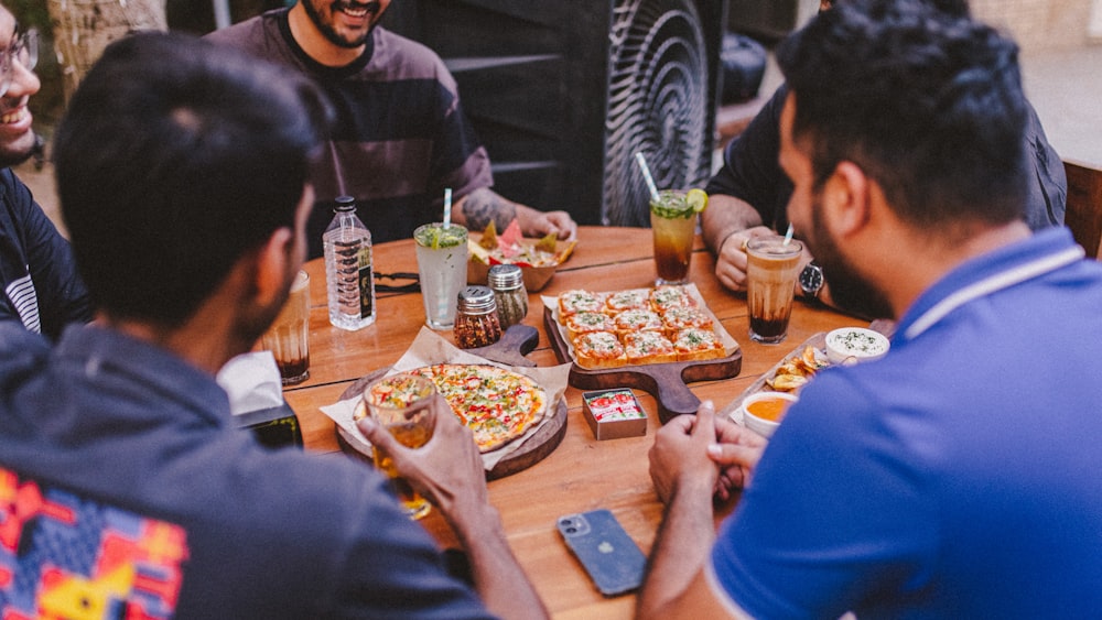 a group of people sitting around a table with pizzas