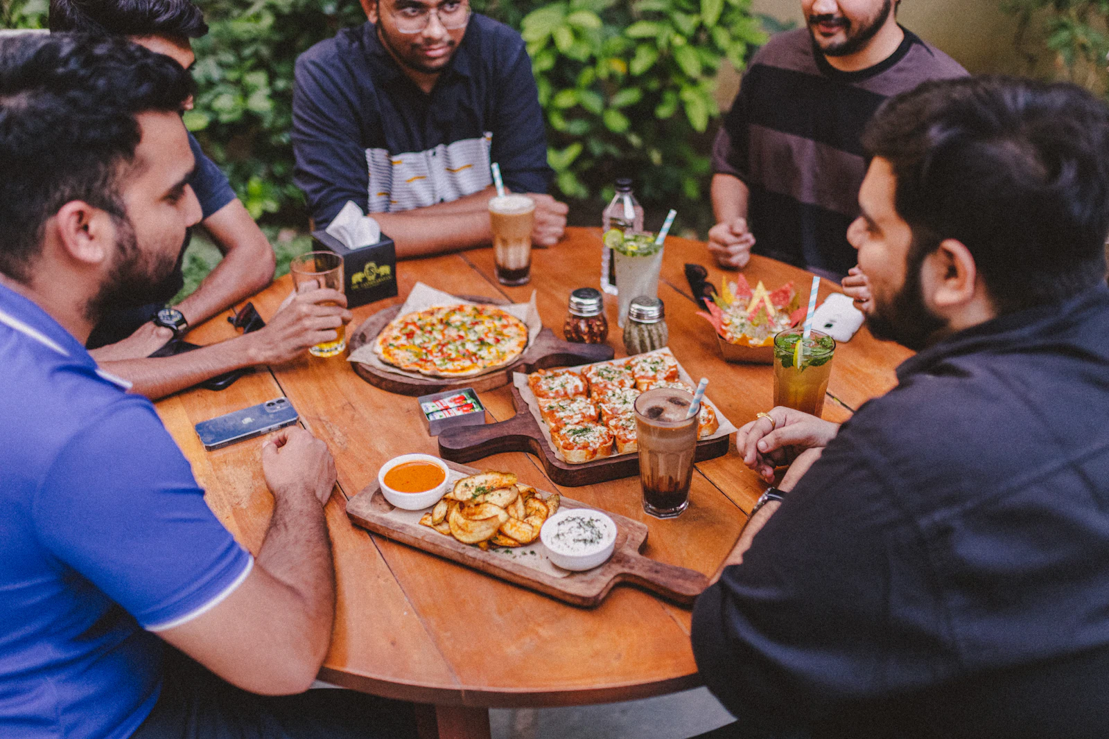 Friends sharing pizzas and drinks around an outdoor café table