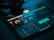 A tablet screen displays a music production software interface with various controls like dials, sliders, and waveform visuals. The background is dark, with illuminated elements in yellow and teal hues. Nearby, a pair of headphones lies on a flat surface.