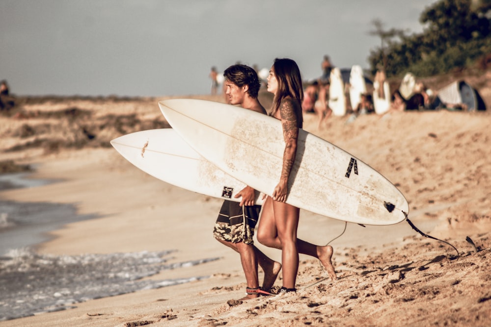 a couple of women walk on the beach carrying surfboards