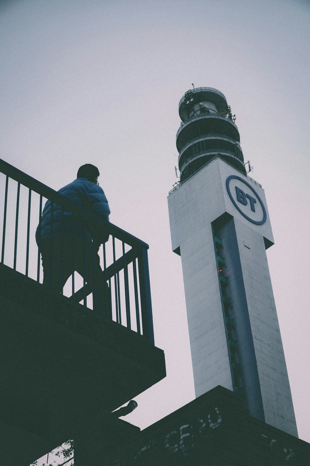 uma pessoa sentada em um corrimão ao lado de uma torre do relógio