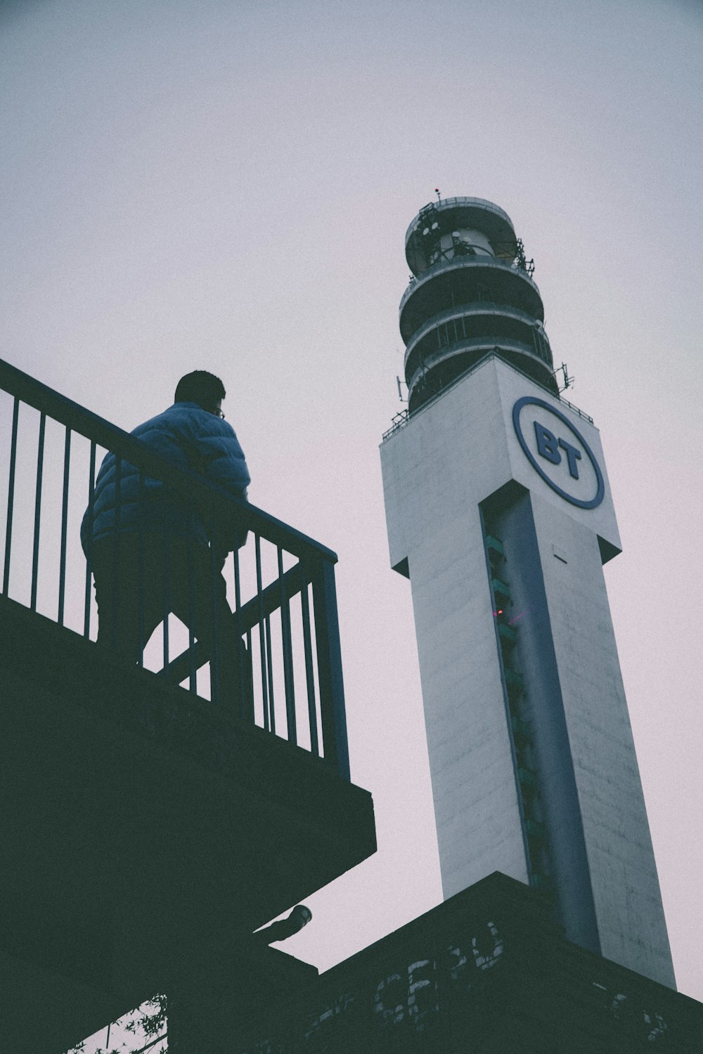 a person sitting on a railing next to a clock tower