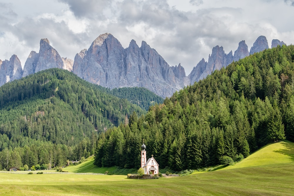 um pequeno edifício branco em um campo gramado com árvores e montanhas ao fundo com Dolomitas ao fundo