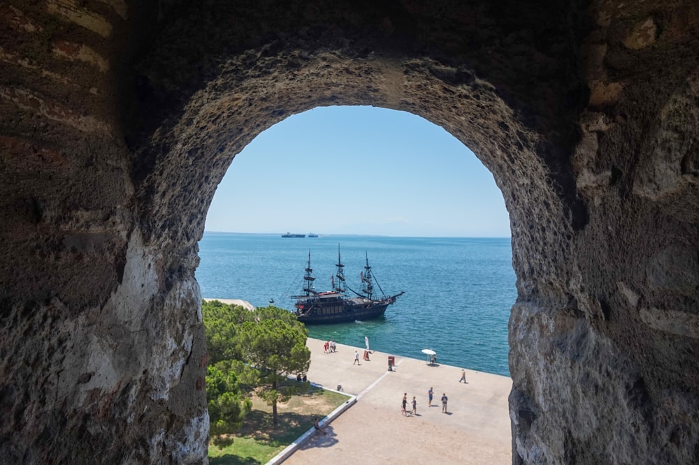 a view of a bay through a stone archway at a beach with boats