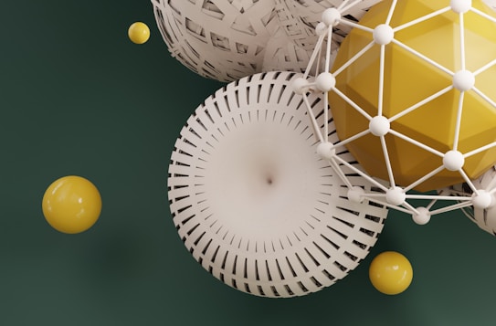 A collection of geometric shapes with intricate patterns and designs, featuring spheres and other spherical forms in a mix of cream and yellow colors. These shapes are set against a dark green background, creating a striking contrast. The structures include a combination of smooth and lattice-like textures.