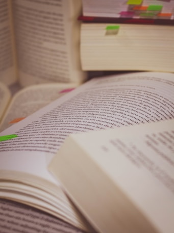 A collection of open books, some with visible text and colorful tabs marking certain pages. The books are arranged haphazardly, suggesting a study session or research activity.