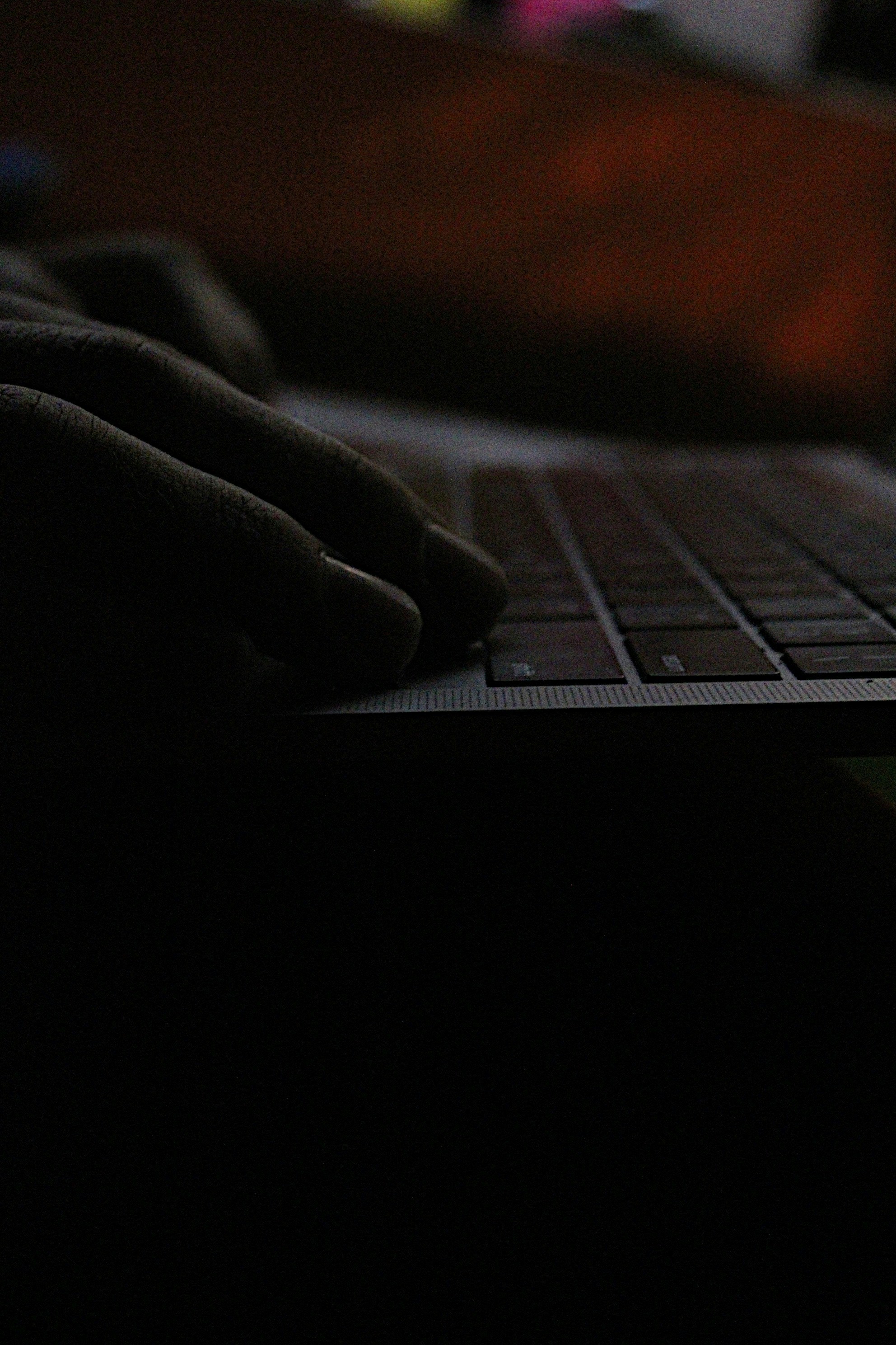 Close-up of hands on laptop keyboard in low ambient light, productive working environment