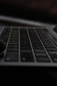 A close-up view of a dark, sleek keyboard with slightly visible keys in dim lighting, giving an impression of modern technology.