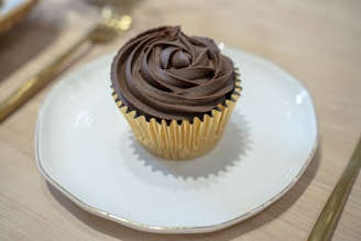 A sophisticated keto cupcake topped with smooth frosting, presented on a polished silver stand.