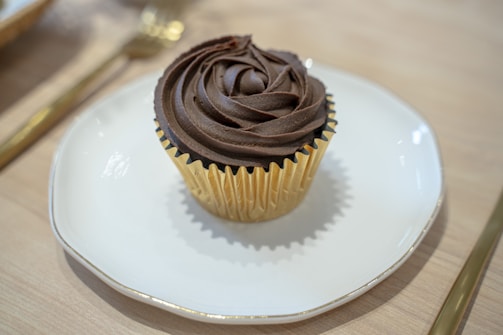 A sophisticated keto cupcake topped with smooth frosting, presented on a polished silver stand.