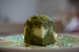 A piece of green and white marble cake sits on a decorative plate with an artistic pattern. The cake has a moist texture and a visually contrasting swirl of colors.